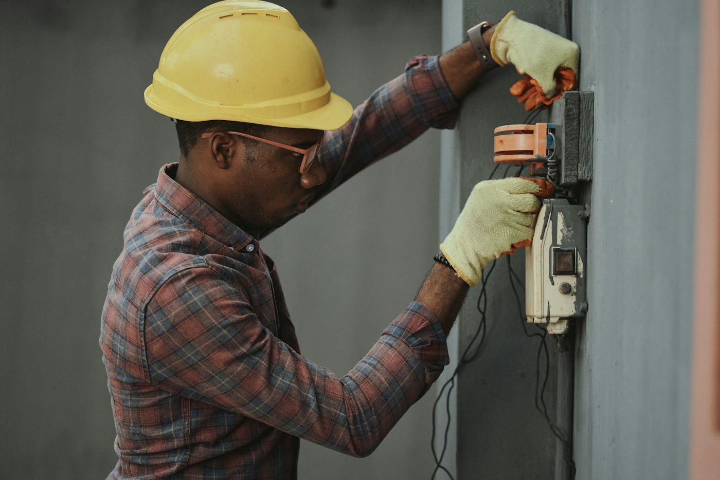 Electrician in a hard hat checking wiring at a wall-mounted electrical box