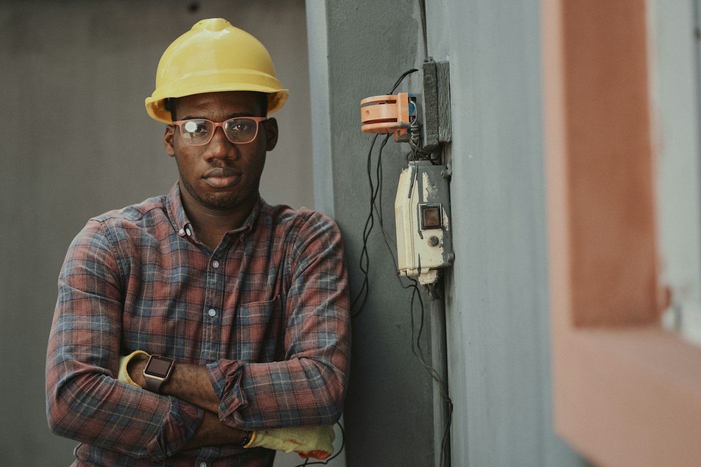 Electrician in a yellow hard hat standing confidently beside an electrical panel