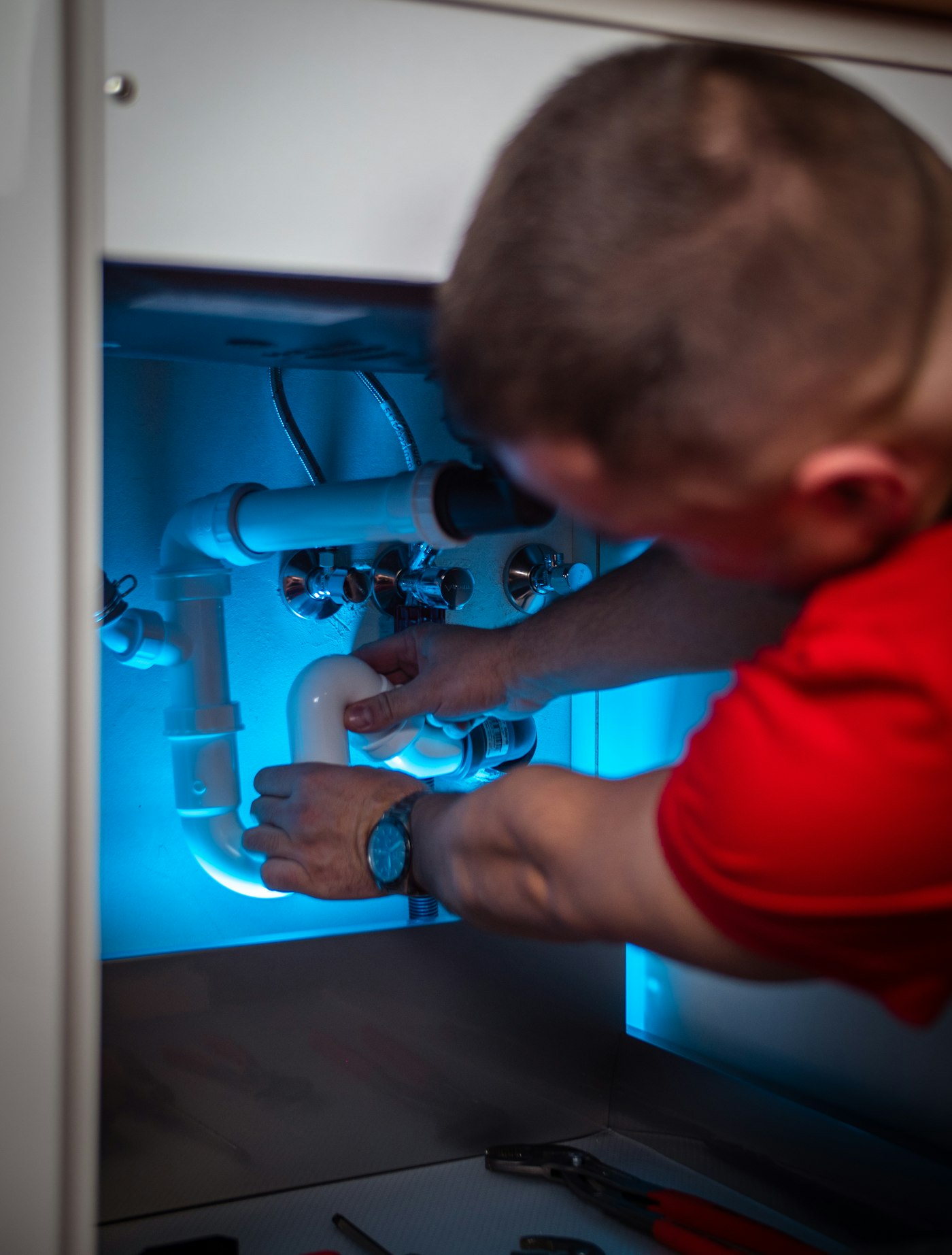 Technician in red gloves repairing a leaking pipe connection under a bathroom basin