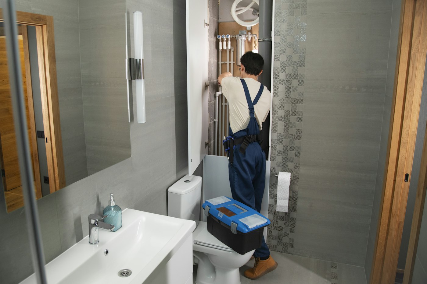Plumbing technician repairing pipework in a tiled bathroom
