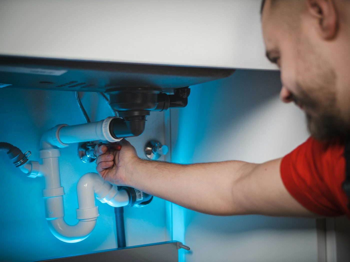 Technician repairing a leaking pipe inside a bathroom vanity cabinet