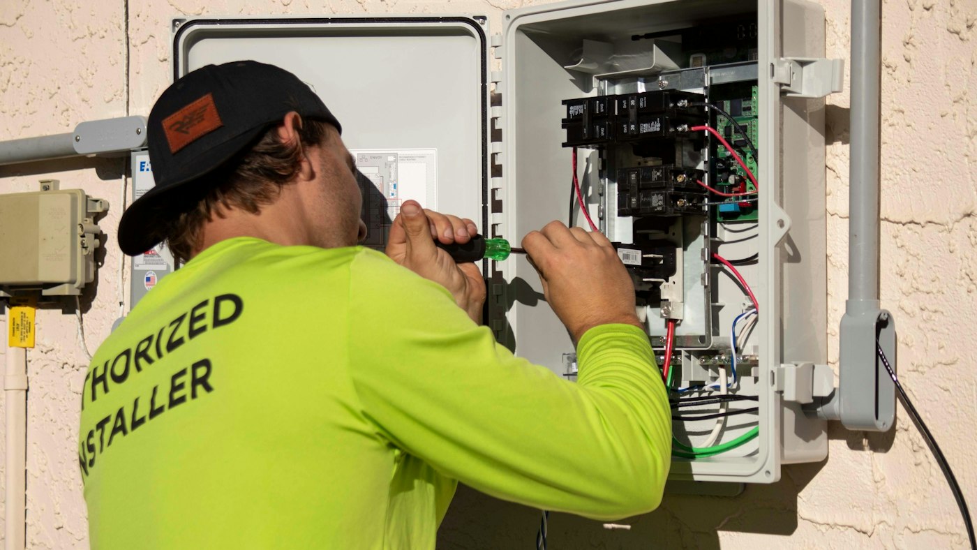 Technician in a high-visibility shirt tightening terminals inside an open electrical distribution panel